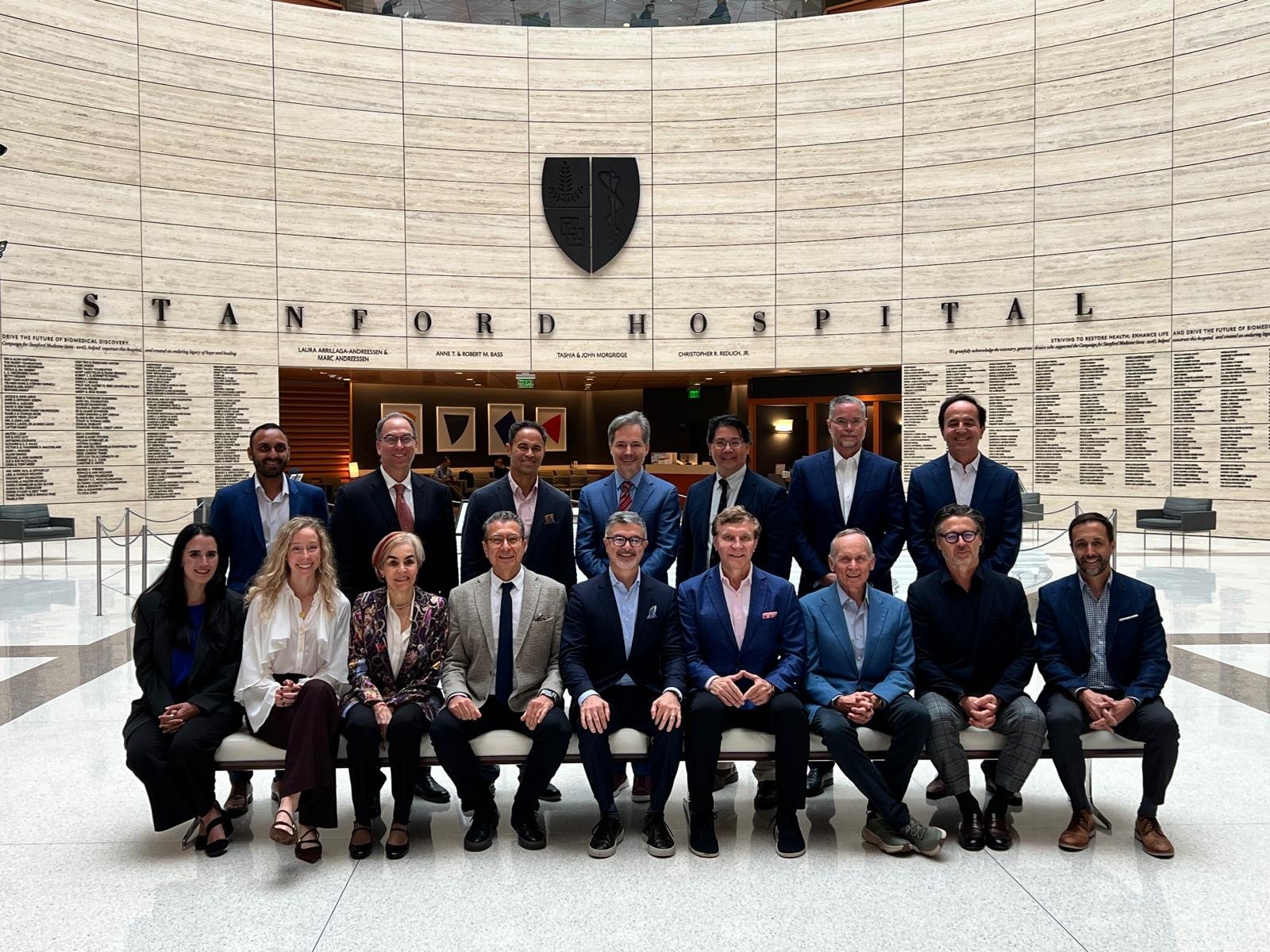 The SPSRC 2025 faculty seated and standing in the atrium of Stanford Hospital beneath the Stanford Hospital sign