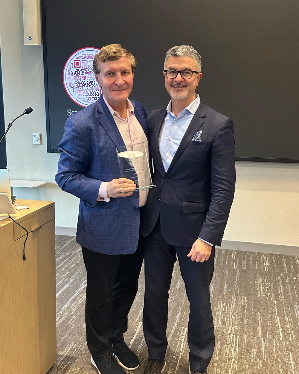 Rod Rohrich holding the SPSRC 2025 Guest of Honor award, standing with Sam Most at the lectern